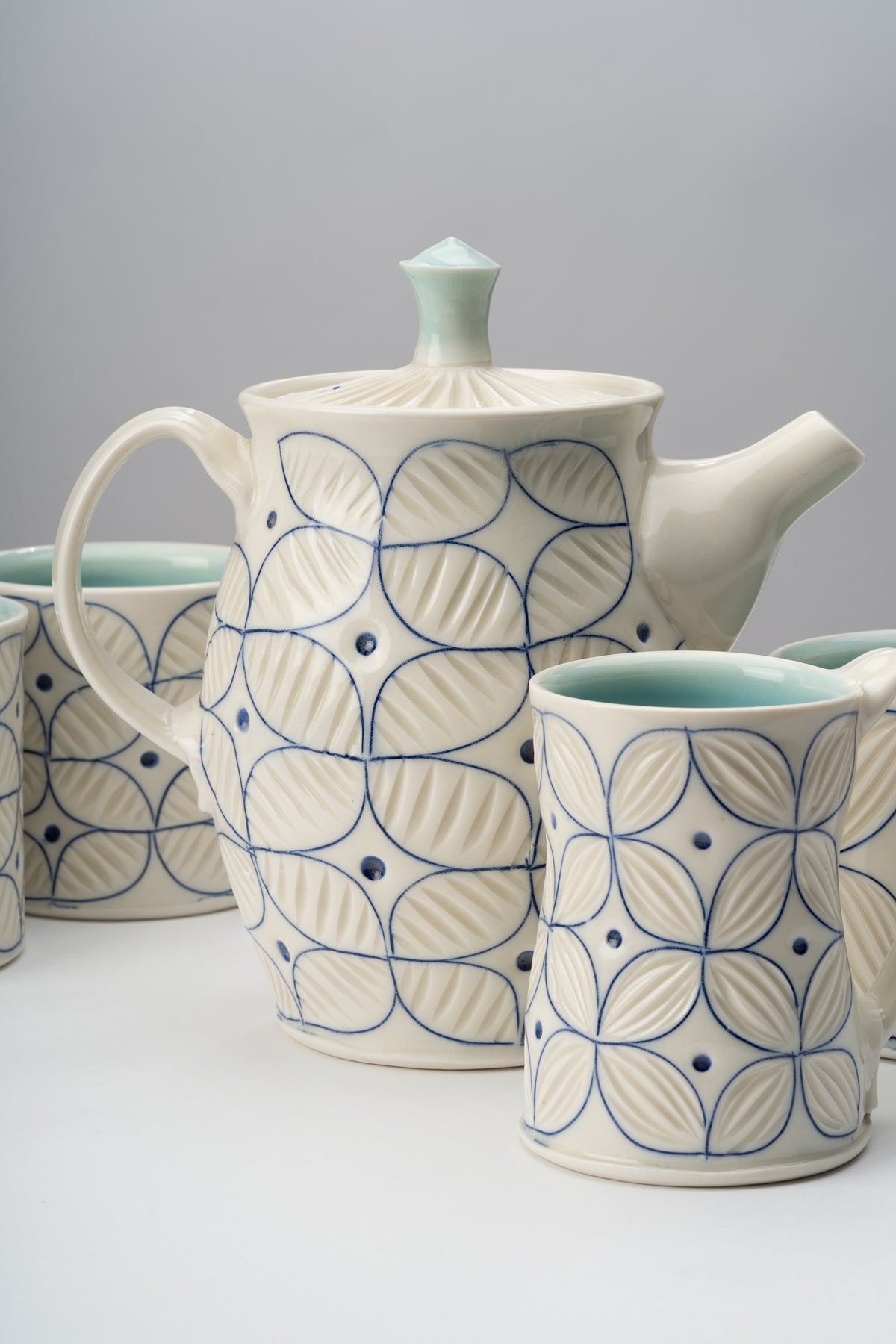 White and blue handmade porcelain cups and a teapot by ceramic artist Julie Wiggins sit on a white table against a grey background. Image by Loam