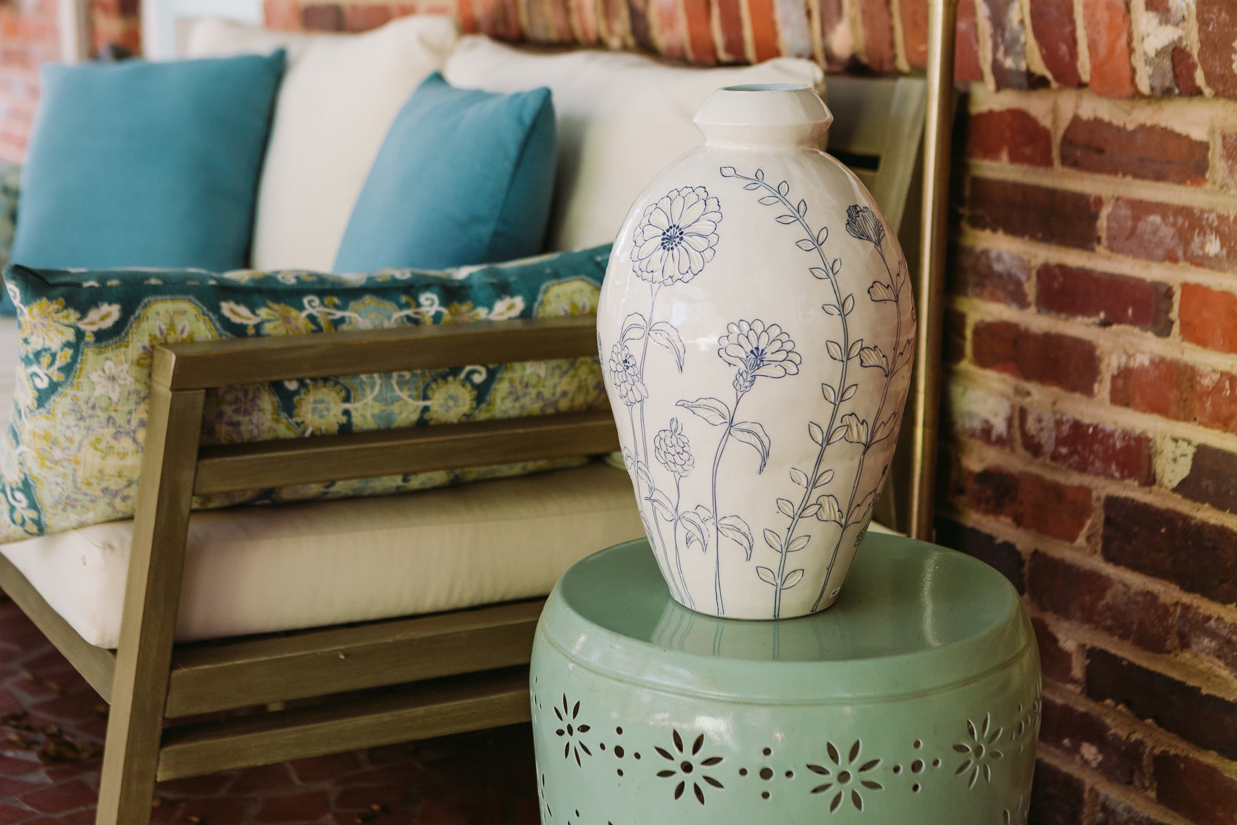 A large handmade porcelain Julie Wiggins vase with cobaly blue floral inlay patterning against an outdoor sitting area background