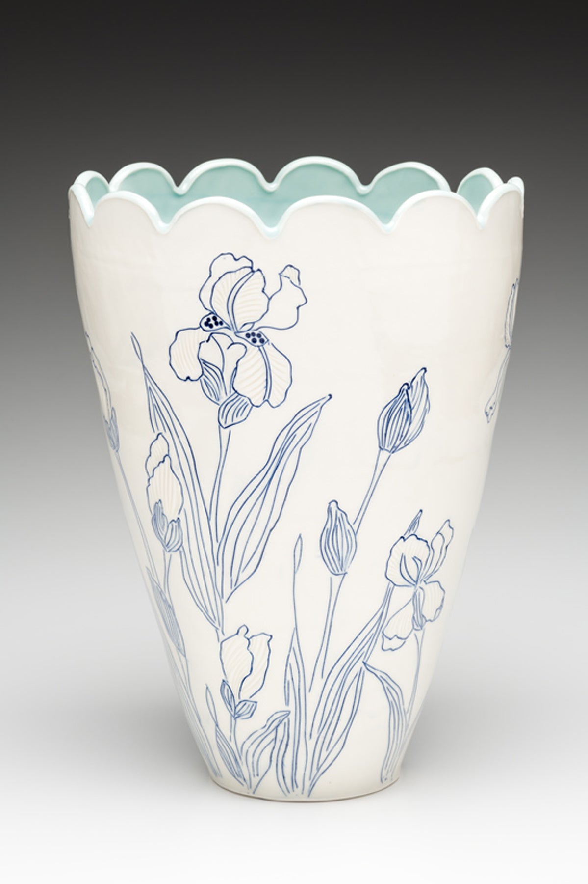 A white handmade porcelain vase with blue inlay by ceramic artist Julie Wiggins sits against a gradient background. 