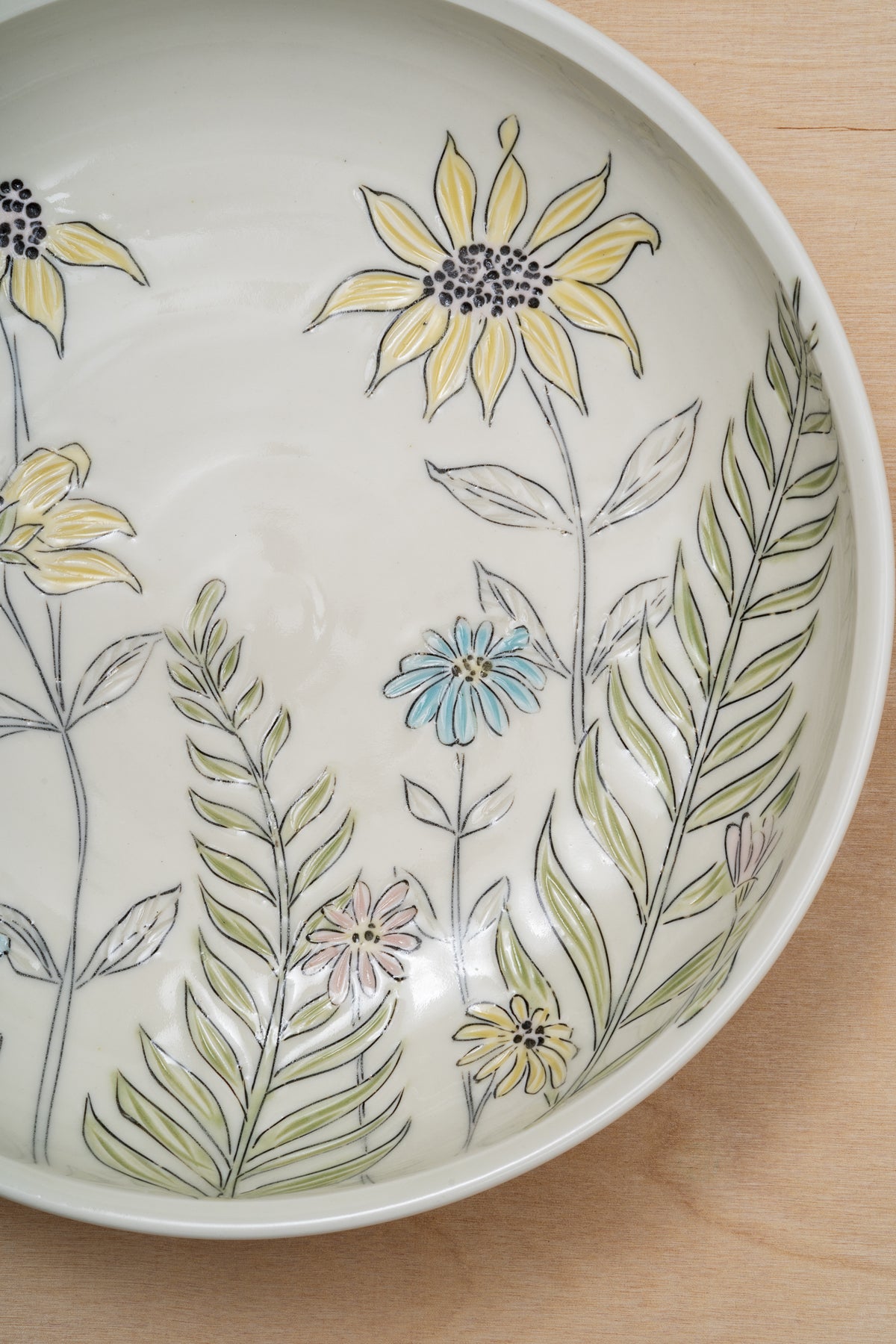 A close up of a serving bowl by artist Julie Wiggins with multicolored floral inlay viewed from above on a light wood table. Image by Loam