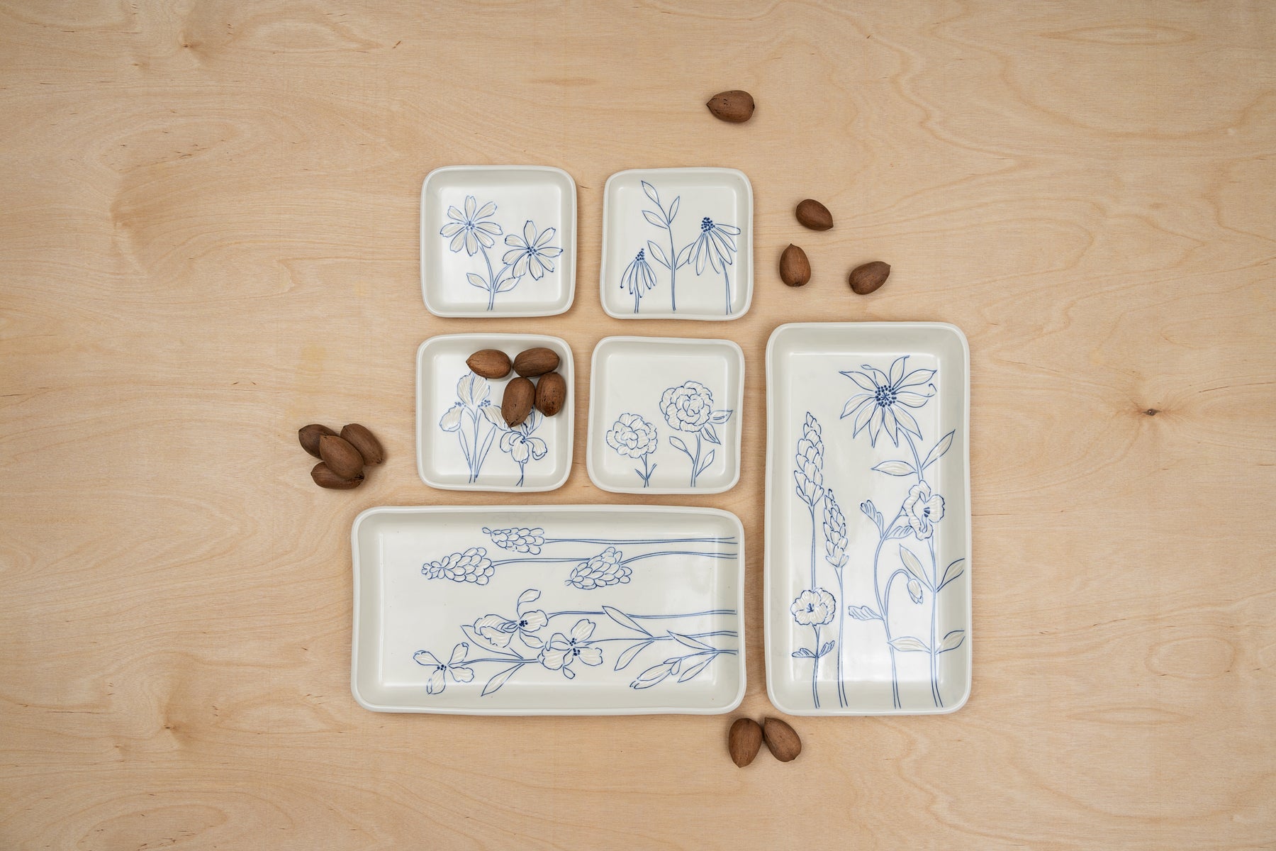 Rectangular and square porcelain plates with blue inlay viewed from above on a table by ceramic artist Julie Wiggins. Unshelled pecans are scattered about the table top