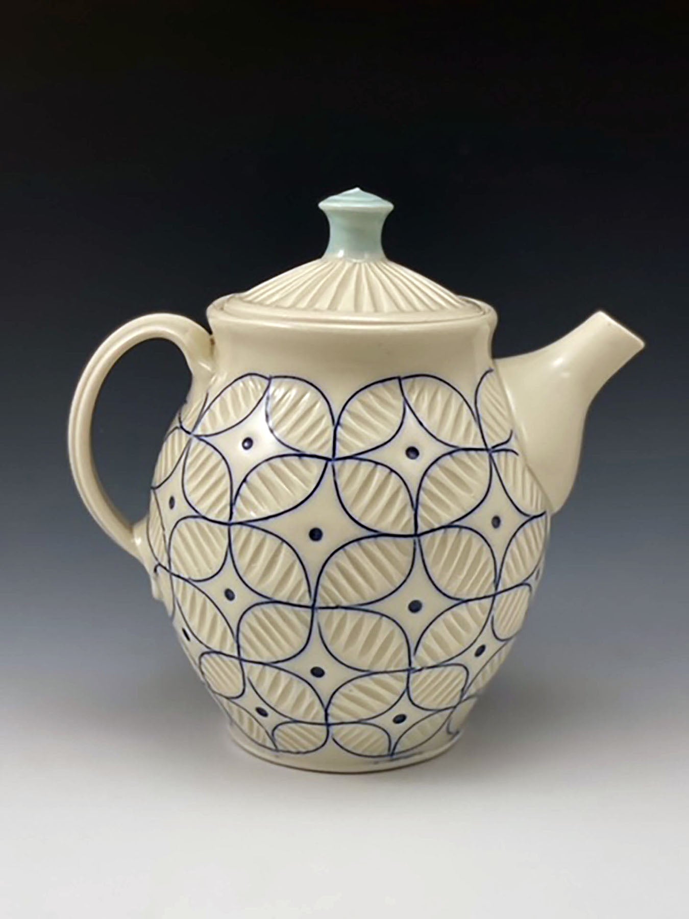 A white handmade porcelain teapot with blue inlay by ceramic artist Julie Wiggins sits against a gradient background. 